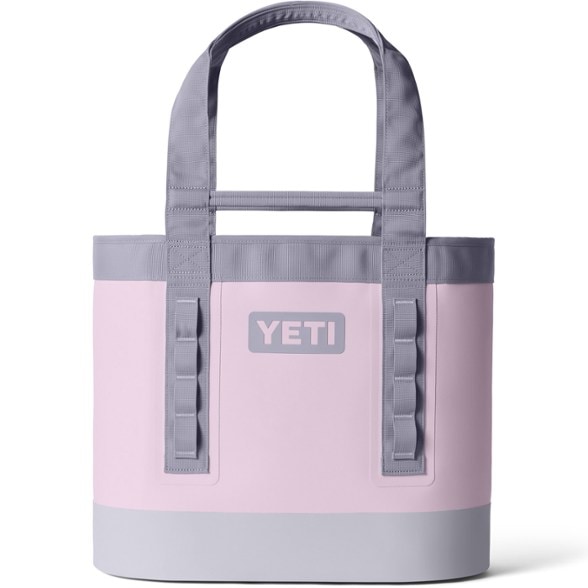 YETI Camino 35 Carryall, a robust dark blue waterproof tote bag, standing upright on a sandy beach with ocean waves in the background, showcasing its durable construction perfect for beach trips.