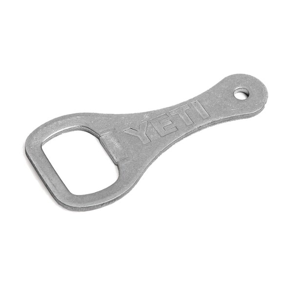 YETI stainless steel bottle opener resting on a camping backpack